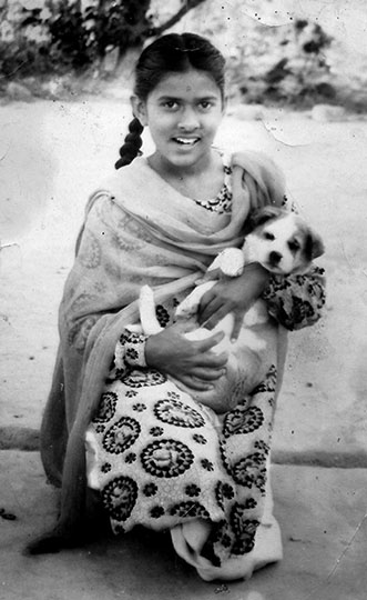 A black and white photograph of Rekha, kneeling down and cradling a puppy.